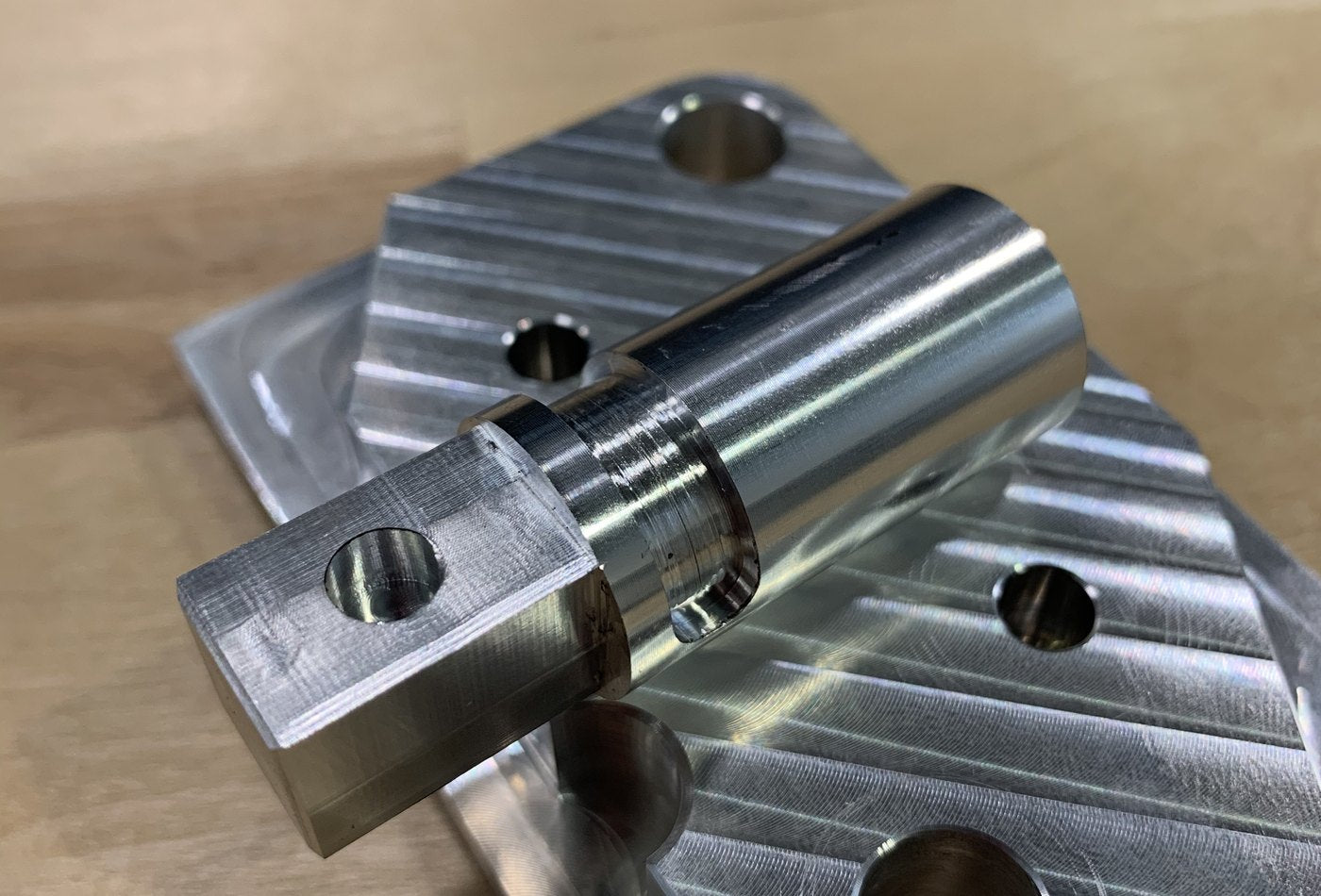 Machined metal plate and turned cylindrical component on a workbench