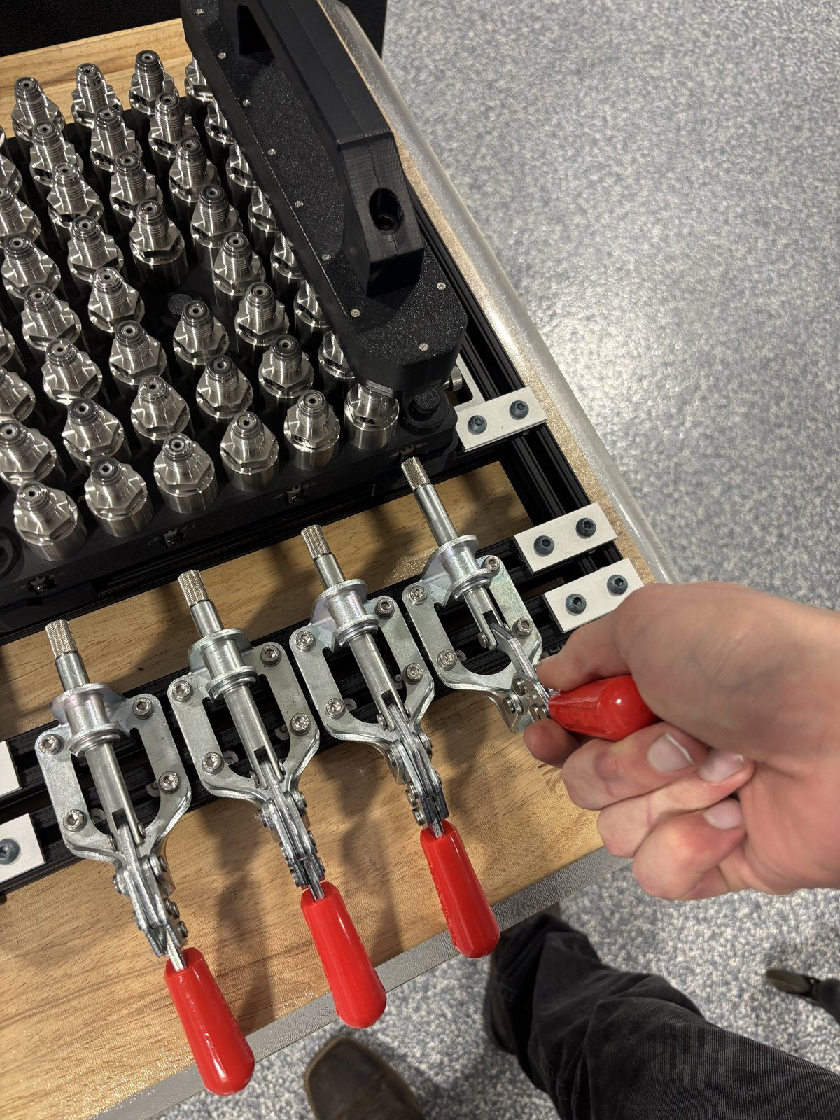 Close view of a red-handled toggle clamp being operated next to the loaded fixture