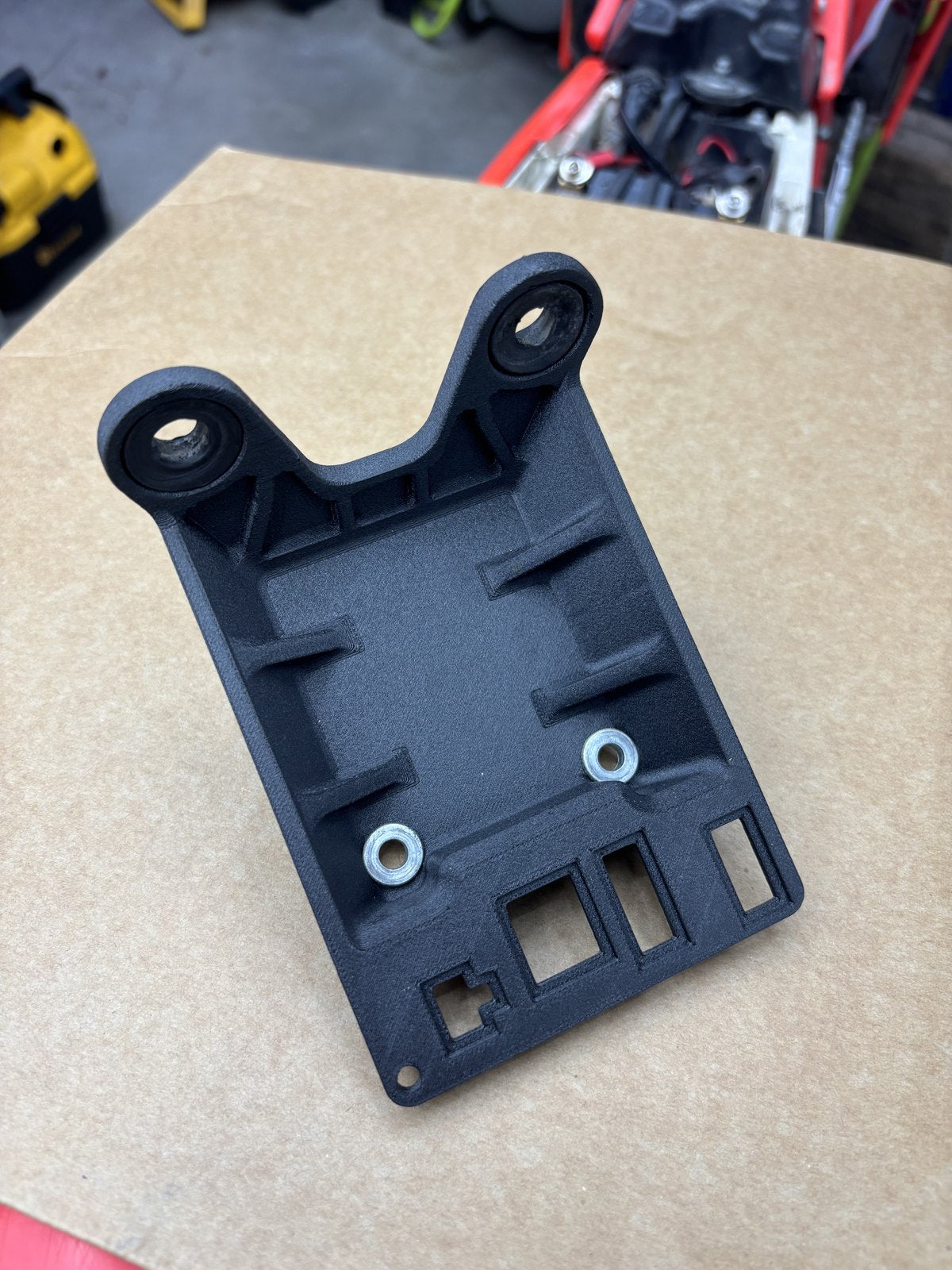 Black display bracket with mounting holes and metal inserts, photographed on a workbench