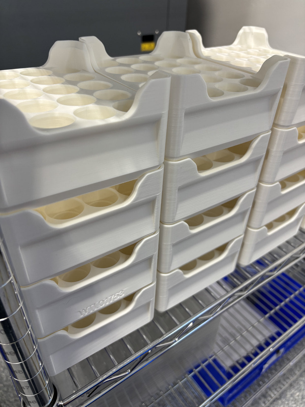 Stacks of white printed trays with repeated circular pockets on a wire shelf